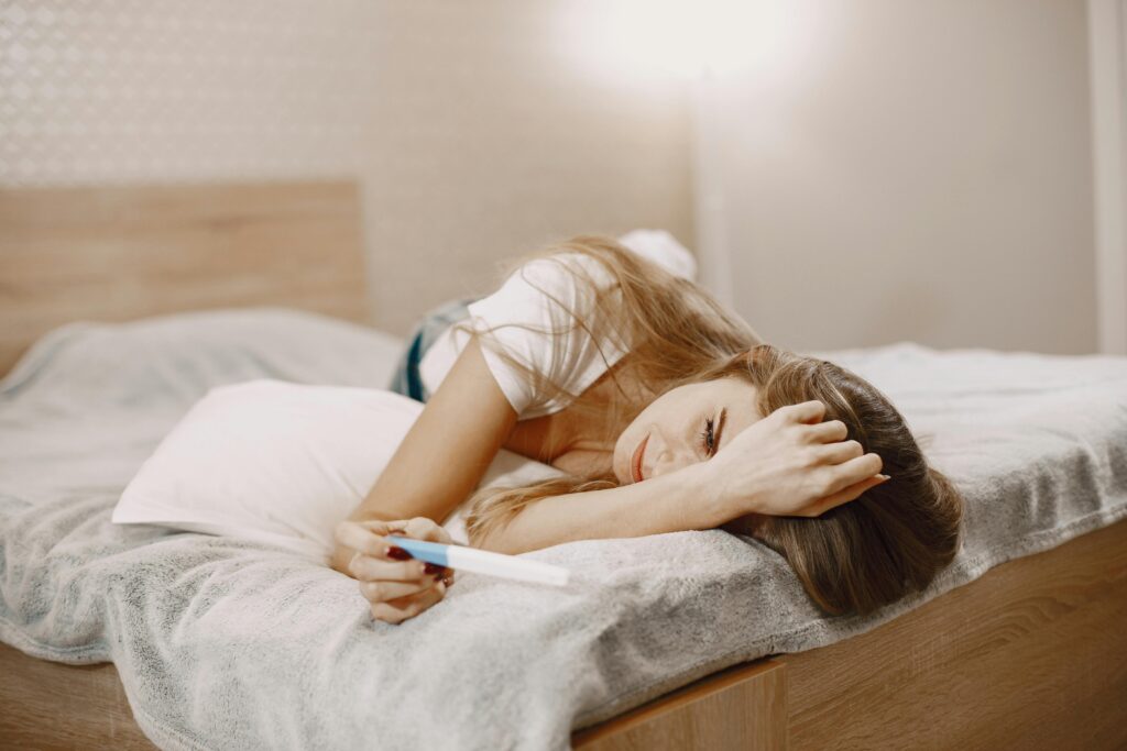 A woman lying on a bed, holding a pregnancy test, contemplating.