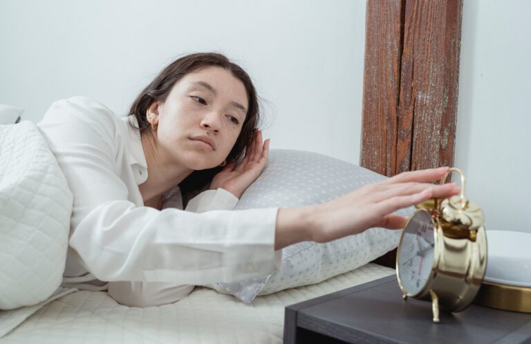 Dlhé zaspávanie, nočné budenie a nepokojný spánok z pohľadu TČM Sleepy young brunette female in white sleepwear resting in comfortable bed and waking up with alarm clock at home in morning time